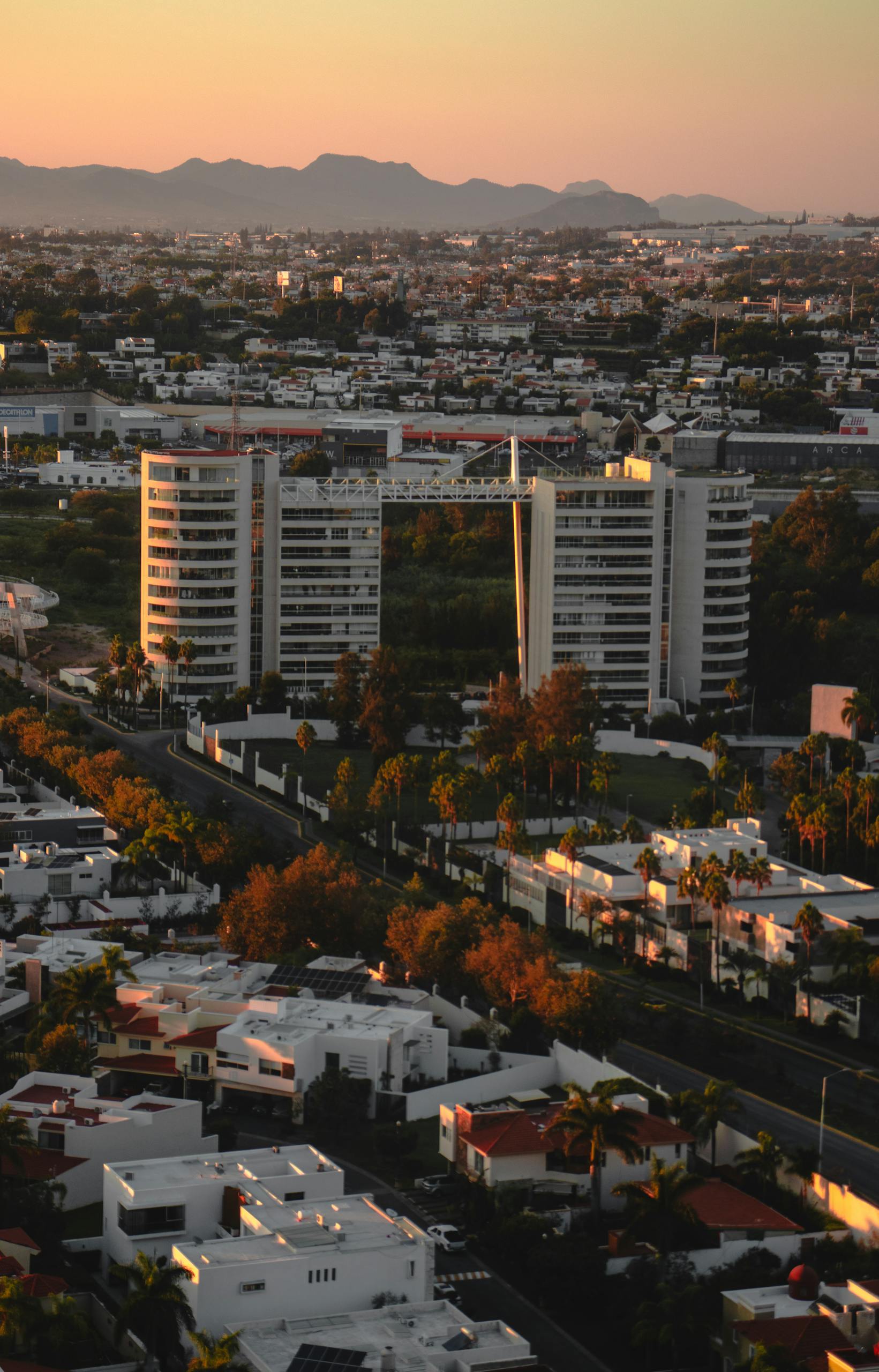 Stunning aerial view of a cityscape at sunset with modern buildings and distant mountains.